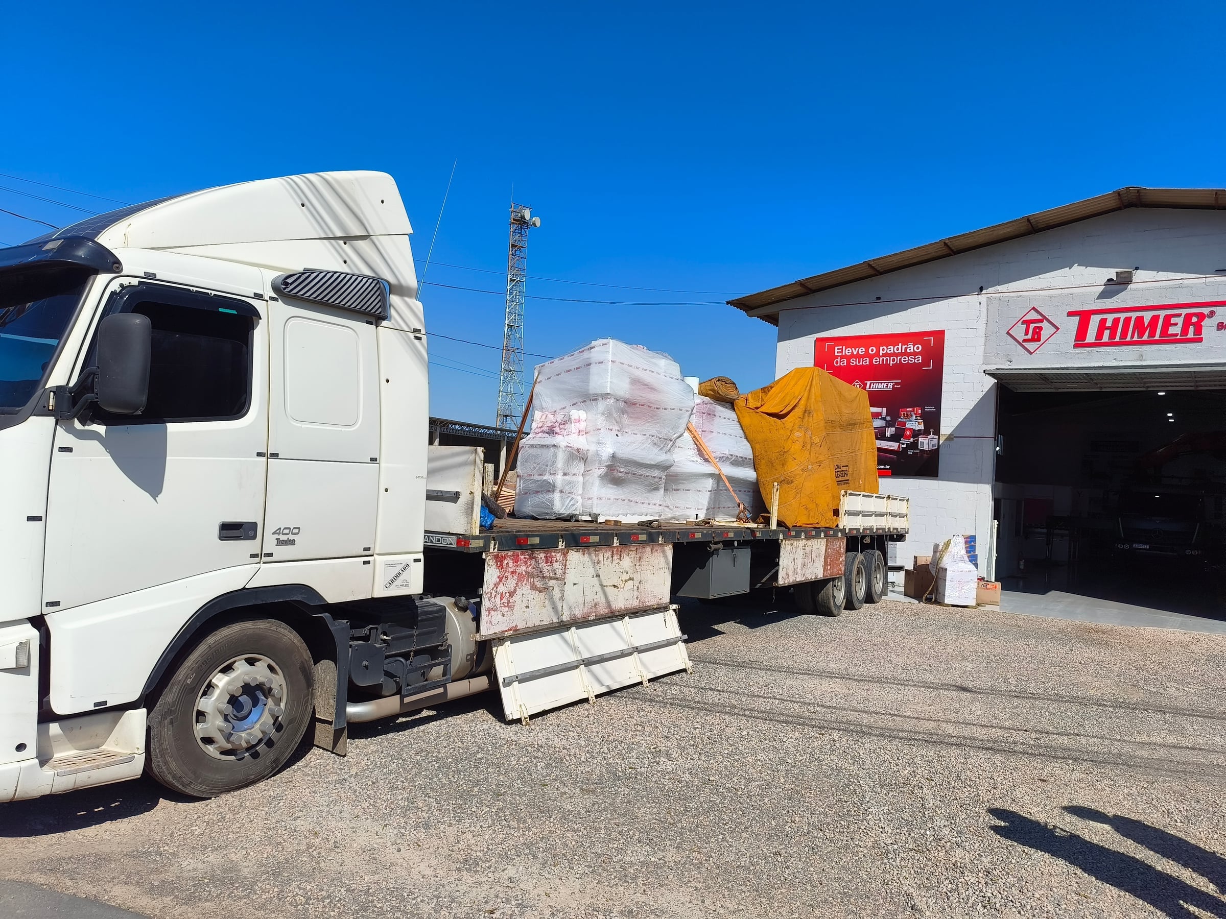 Carreta da A&G carregada com uma máquina industrial amarela, estacionada no pátio do cliente